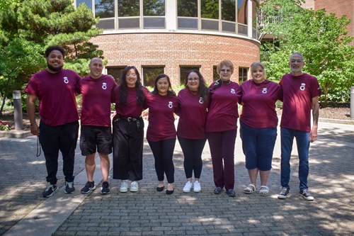 Group of staff standing in a row wearing burgundy with a smile